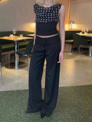 kostymbyxor  - Säljer ett par svarta kostymbyxor med låg midja och breda ben. Byxorna har en unik spetsdetalj i midjan som ger en cool twist till den klassiska looken. Perfekta för dig som vill ha något stilrent men ändå trendigt. Materialet ser ut att vara en mjuk och följsam textil.