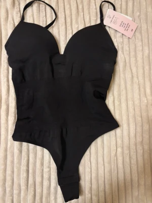 Svart body - Svart body med smala axelband och shaping effekt. Helt ny med lappen kvar. 
