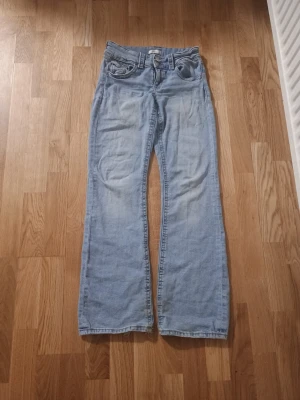 Ljusblå bootcut jeans - Säljer ett par ljusblå bootcut jeans med klassisk femficksdesign och dragkedja. Jeansen har en avslappnad passform och är tillverkade i mjuk denim. Perfekta för en casual och trendig look.