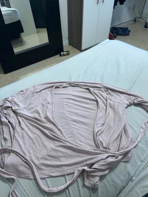 Ljusrosa morgonrock från 157 - Mysig och tunn ljusrosa morgonrock från 157 i storlek XL. Modellen är öppen framtill med knytskärp i midjan och långa ärmar. Perfekt för chill dagar hemma och enkel att slänga på sig över pyjamasen.