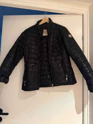 Svart pufferjacka från Moncler - Snygg svart pufferjacka från Moncler med quiltad design och hög krage.  Den är lite förstor för min smak där av jag säljer den. 