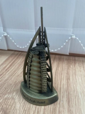 Souvenir Burj Al Arab modell - Säljer en liten souvenir i metall som föreställer Burj Al Arab Hotel. Modellen är guldfärgad med detaljer och texten 'Burj Al Arab Hotel' på basen. Perfekt som prydnad eller samlarobjekt för dig som gillar arkitektur eller Dubai.