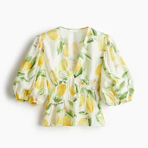 Vit blus med citronmönster - Helt ny köpt och Superfin vit blus med färgglatt citronmönster och gröna blad. Blusen har v-ringning, puffiga trekvartsärmar och smockad midja som ger en snygg siluett. Perfekt för dig som vill sticka ut med en fräsch och somrig vibe!