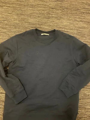 Mörkblå sweatshirt från A Day's March - Klassisk mörkblå sweatshirt från A Day's March med rund halsringning och ribbade muddar vid ärmslut och nederkant. Perfekt basplagg i mjukt material som funkar till allt. Enkel och stilren design utan tryck eller mönster.