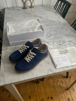 Blå sneakers Maison Margiela - Säljer ett par helt nya Masion margiela gats i en riktigt snygg blå färg, i stl 43! Skorna är helt oanvända (endast prövade). Och kommer komplett med box, dustbag och alla tillbehör som syns på bilderna. Kom med bud! Hör av dig vid frågor eller funderingar!