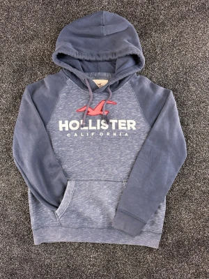 Blå/grå vintage hoodie från Hollister - Blå/grå vintage hoodie från Hollister. Fint skick. Storlek small, men funkar även som medium. Vid frågor är det bara att höra av sig. 