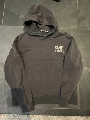 Svart hoodie One Tribe - Svart hoodie från One Tribe med tryck på bröstet. Klassisk modell med huva och känguruficka framtill. Tillverkad i mjukt bomullsmaterial och har ribbade muddar vid ärmslut och nederkant. Perfekt för en avslappnad och street-inspirerad stil.