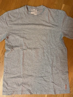 Grå t-shirt från Acne Studios - Klassisk grå t-shirt från Acne Studios i mjuk bomull. T-shirten har rund halsringning, korta ärmar och en liten diskret logga nere vid fållen. Perfekt basplagg för alla tillfällen.
