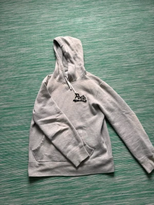 Grå hoodie från Polo Ralph Lauren - Snygg grå hoodie från Polo Ralph Lauren med broderad svart logga och texten 'EST. 1967' på bröstet. Hoodien har känguruficka, dragsko i huvan och är tillverkad i mjukt bomullsmaterial. Perfekt för en avslappnad och trendig stil.passar dig runt 165-175 cm 