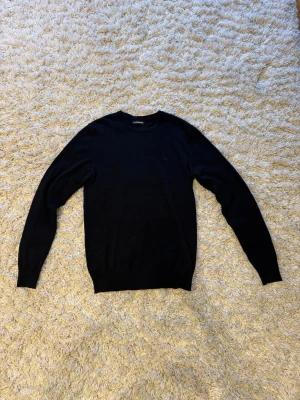 Svart merino J.Lindberg tröja - En skitsnygg J.Lindberg tröja i merino ull. Tröjan är i storlek M men sitter även bra på S. Tröjan är tunn, luftig och passar till nästan allt. Perfekt till sommaren! Tagen har lossnat på höger sida men det är inget som påverkar och det är enkelt att fixa. 