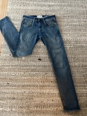 Blå Replay Anbass jeans - Snygga blå slim fit jeans från Replay med klassisk femficksdesign och diskreta slitningar framtill. Jeansen har normal midja och smala ben, perfekta för en trendig och avslappnad look. Tillverkade i mjukt denimtyg för skön passform. Waist 27 length 32. 