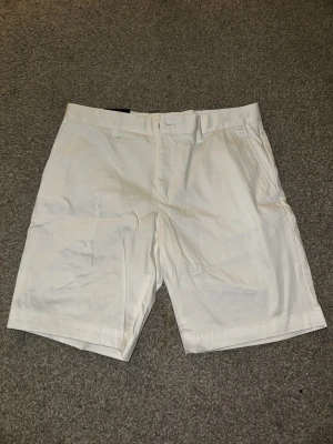 Vita satinshorts från J.Lindeberg - Snygga vita shorts från J.Lindeberg i satinmaterial. Storlek 31 men passar också 33. Klassisk rak passform med bälteshällor och diskreta fickor. soprena och stilrena shorts som passar perfekt till sommaren. Skriv över det minsta lilla eller över den minsta funderingen!🔥🔥