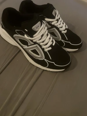 Dior b30 - Säljer ett par Dior B30 sneakers i svart och vitt. Skorna har en chunky sula, vita snören och coola reflekterande detaljer. Märket syns tydligt på plösen och designen är sportig med futuristiska inslag. Perfekta för dig som gillar exklusiva och trendiga sneakers.