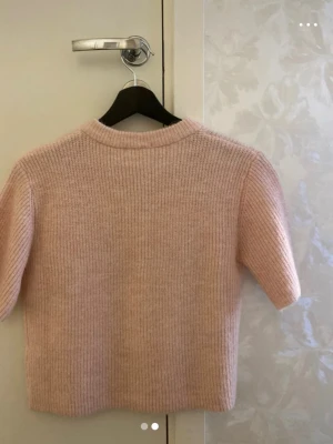 Ljusrosa stickad kortärmad kofta - Söt ljusrosa stickad kofta med korta ärmar och rund hals. Koftan har ribbstickad struktur och knäpps med matchande knappar framtill. Perfekt att slänga över en topp för en mysig och trendig look.