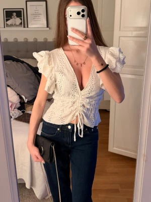 Vit blus med volang och snörning - Supersöt vit blus med broderade detaljer, volangärmar och  v-ringning. Står att det är en L men jag kan ha den och är en xs/ s. 