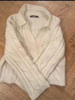 Vit kabelstickad tröja med krage - Säljer en vit kabelstickad tröja från Bik Bok med bred krage och v-ringning. Tröjan har långa ärmar och ribbade muddar vid ärmslut och nederkant. Perfekt för lager på lager och riktigt mysig till kyliga dagar.