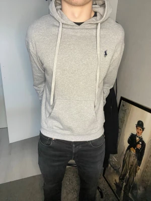 Grå hoodie från Polo Ralph Lauren - Snygg grå hoodie från Polo Ralph Lauren med klassisk logga broderad på bröstet. Hoodien har huva med dragsko och en stor magficka. Mjuk bomullskänsla och ribbade muddar vid ärmslut och nederkant. Perfekt för chill dagar./ passar mig som egentligen har M! 