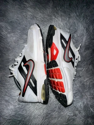 Nike vita och svarta sneakers - Nike sneakers i vitt med svarta och röda detaljer. Skorna har en klassisk låg silhuett, meshpaneler för ventilation och en tydlig röd Swoosh på sidan. Yttersulan har svarta och röda partier för extra grepp. Perfekta för en sportig och trendig look.