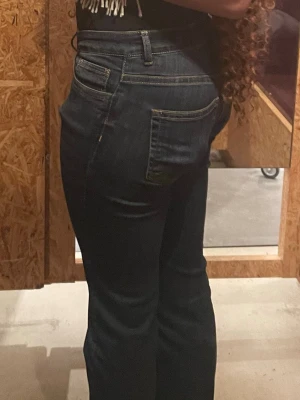 Mörkblå bootcut jeans med knappar - Snygga mörkblå bootcut jeans med hög midja och fyra synliga knappar framtill. Jeansen har klassiska fickor både fram och bak samt bälteshällor. Materialet är stretchigt denim som sitter bekvämt och formar sig efter kroppen.