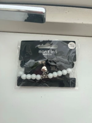 Vitt och svart pärlarmband från Montini - Oöppnade och oanvända snygga armband från Montini med vita och svarta runda pärlor och silverfärgade detaljer. Armbanden har även en liten hängande berlock i form av ett hjärta med magnet och dekorativa metallpärlor. Perfekt accessoar för att lyfta din stil.