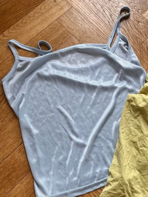 Ljusblå ärmlös linnetopp - Säljer en enkel och stilren ljusblå linnetopp med tunna axelband. Toppen har en rak passform och är tillverkad i ett mjukt, stretchigt syntetmaterial som känns skönt mot huden. Perfekt att matcha med jeans eller kjol för en avslappnad look.Skriv gärna för mått! 💕