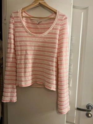Rosa-vit randig stickad topp - Säljer denna topp med rosa och vita ränder från Nelly. Modellen har lång utsvängd (synd dock ej på bilden)  ärm och rund halsringning. Perfekt för dig som gillar pastell och en avslappnad vibe. Materialet känns mjukt och ger en skön känsla. Endast använd en gång. 😊