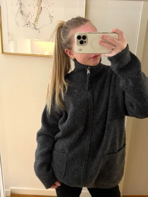 Mörkgrå zip vårjacka Zara - Mysig mörkgrå cardiganjacka med dragkedja framtill och två stora fickor. Jackan har hög krage och är tillverkad i ett mjukt, stickat material som ger en avslappnad och oversized look. Perfekt för våren