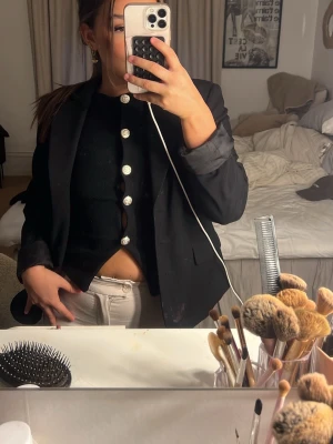 Svart stickad väst med knappar - Snygg svart stickad väst med stora silvriga knappar framtill. Västen är ärmlös och har en croppad passform som ger en trendig look. Perfekt att styla över en skjorta eller bära som den är för en cool vibe.