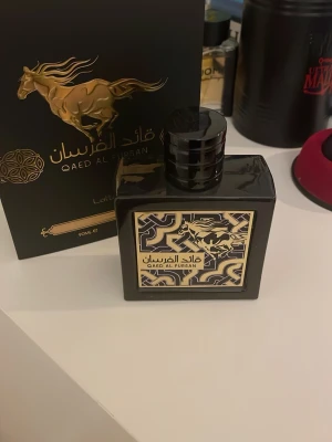 Qaed Al Fursan Eau de Parfum 90ml - Qaed Al Fursan Eau de Parfum från Lattafa i en elegant svart glasflaska med gulddetaljer och ett unikt mönster på etiketten. Flaskan rymmer 90 ml och har en lyxig design med en guldhäst på förpackningen. Tillverkad i Förenade Arabemiraten. 90% kvar 