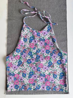 Blommig topp från Bikbok, storlek S - Säljer en färgglad topp från Bik Bok i storlek S. Toppen har ett blommigt mönster med vita detaljer. Den är ärmlös och har knyt i nacken. Aldrig använd.