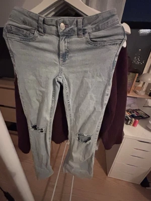 Nelly jeans - Säljer ett par ljusblå jeans med slitningar vid knäna och coola rosa broderade detaljer på bakfickorna. Jeansen har klassisk femficksmodell och är i stretchigt denimtyg. Perfekta för en avslappnad och trendig look.