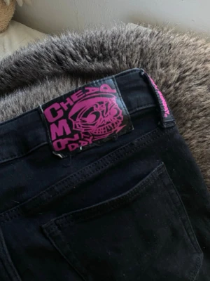 Weekday - Säljer ett par svarta jeans från weekday med coolt rosa märke på bakfickan och slitna detaljer vid knäna. Jeansen har klassisk femficksdesign och är tillverkade i denim med stretch för skön passform.