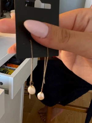 Långa örhängen med pärlor - Säljer ett par stilrena örhängen med tunna kedjor i silverfärg och vita pärlor längst ner. Perfekta för dig som gillar minimalistisk och elegant stil. Örhängena har en modern look och passar till många olika outfits.