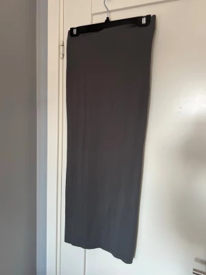 Mörkgrå långkjol i stretchigt tyg - En enkel och stilren mörkgrå långkjol i ett stretchigt och mjukt material. Kjolen har en rak passform och är perfekt för dig som gillar minimalistisk stil. Inga synliga detaljer eller mönster, bara clean och snygg.