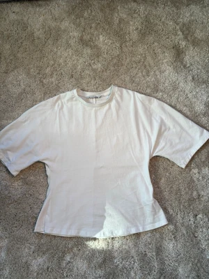 Vit figursydd t-shirt i bomull - En enkel och stilren vit t-shirt med figursydd passform och längre ärmar. Tillverkad i mjuk bomull och har en klassisk rund halsringning. Perfekt basplagg för alla tillfällen och lätt att matcha med andra plagg.