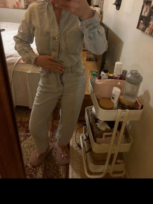 Ljusblå denim jumpsuit med fickor - Säljer en ljusblå denim jumpsuit med dragkedja och knappar framtill. Modellen har långa ärmar med resår vid handlederna, stora bröstfickor och dragsko i midjan för en snygg passform. Perfekt för dig som gillar en avslappnad men trendig look. Säljer denna fina byxdress från Zara i jeans❣️Perfekt inför våren och jag säljer då den inte passar mig. Storlek S på den och jag är 162 cm. Endast testad enstaka gånger och den är nytvättad❣️