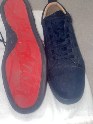 Mörkblå sneakers från Christian Louboutin - Snygga mörkblå sneakers i mocka från Christian Louboutin med klassisk röd sula och matchande mörkblå skosnören. Låg modell med diskreta sömmar och stilren design. Perfekta för dig som vill ha något exklusivt och trendigt.