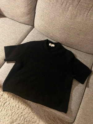 Svart stickad t-shirt - Kortärmad svart stickad t-shirt med rund halsringning och avslappnad passform. Perfekt för lager på lager och enkel att styla till olika looks.