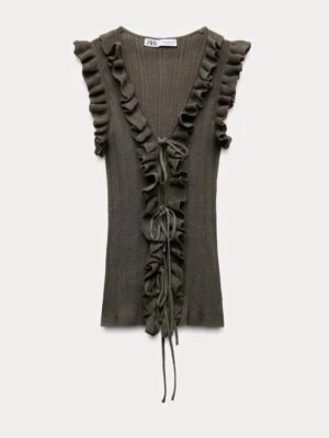 Brun ribbad topp med volang från Zara - Supersnygg brun ribbad topp från Zara med volangdetaljer längs v-ringningen och framtill. Toppen är ärmlös och har knyt framtill för extra stilpoäng. Perfekt att styla med jeans eller kjol för en trendig look.