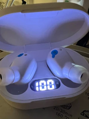 Vita trådlösa in-ear hörlurar - Säljer ett par vita trådlösa in-ear hörlurar med laddningsetui och digital display som visar batterinivå. Hörlurarna har en kompakt och stilren design med silikontoppar för bekväm passform. Perfekta för musik, poddar och samtal på språng.