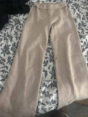 Beiga mjuka loungewear-byxor - Mysiga loungewear-byxor i beige med bred resår i midjan. Tillverkade i ett fluffigt och mjukt material som känns skönt mot huden. Perfekta för att chilla hemma eller ha en avslappnad dag. Vida ben för extra komfort.