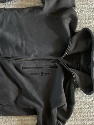 Svart hoodie Sail Racing med dragkedja - Säljer en svart hoodie från Sail Racing med dragkedja framtill och en extra ficka med zip på bröstet. Hoodien har en stilren design och är tillverkad i ett mjukt material. Perfekt för dig som gillar sportig och clean stil.