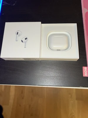 Apple AirPods med laddningsetui - Säljer ett par vita Apple AirPods med Lightning-laddningsetui. Snygg och stilren design i plast, perfekt för dig som vill ha trådlösa hörlurar med bra ljud och enkel anslutning till iPhone eller andra Apple-enheter. Kommer i originalförpackning.