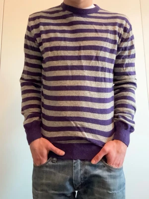 Lila och grårandig tröja Baldini - Stickad tröja från Baldini med lila och grå horisontella ränder. Tröjan har rund halsringning, ribbade muddar och nederkant. Perfekt för dig som gillar en avslappnad men ändå stilren look.