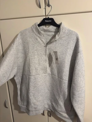 Grått mjukisset - Säljer ett grått mjukisset med en halvzip tröja och matchande sweatpants. Tröjan har hög krage och dragkedja, byxorna har resår i midjan och fickor. Båda i mjukt bomullsmaterial, perfekta för chill eller träning. OBS TAGGAR SÄGER XXL MEN PASSAR INTE XXL PÅRIKTIGT. DET ÄR MER FÖR L ELLER M STORLEK