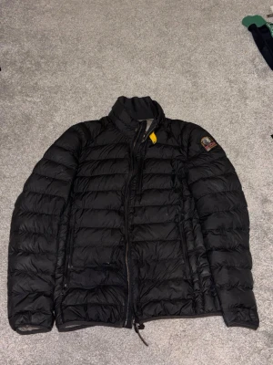 Svart pufferjacka från Parajumpers - Säljer en svart pufferjacka från Parajumpers med gul detalj vid kragen och patch på ärmen. Jackan har hög krage, två sidofickor med dragkedja och quiltad design. Insidan är ljusgrå och materialet är lätt och värmande, perfekt för kalla dagar.