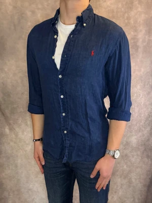 Marinblå Ralph Lauren Linneskjorta - Stl S, Slim fit - RIKTIGT FET LINNESKJORTA FRÅN RALPH LAUREN I FÄRGEN Marinblå med röd pony, perfekt till sommaren som närmar sig! 🏖️🌊 | Mycket bra skick: 9,5/10, utan defekter! | Stl: S |  Modellen är 176cm och väger 75kg,  | Hör av dig vid frågor // Galgen 🫡