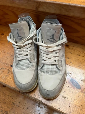  Air Jordan 4  - Säljer ett par Off-White x Air Jordan 4 Sail sneakers i beige och vitt. Skorna har meshpaneler, klassiska Off-White detaljer som texten 'AIR' på sidan och signatur-Jumpman logga på plösen. Tillverkade i läder och mesh med högt skaft och vita skosnören.