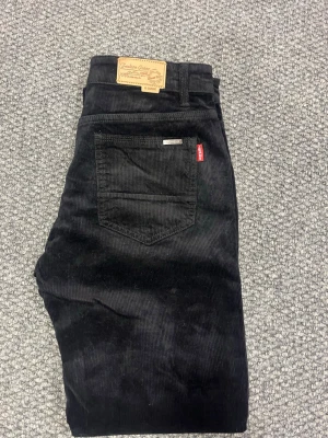 Svarta jeans manchesterbyxor - Säljer ett par svarta manchesterbyxor från Lindex med klassisk femficksmodell och raka ben. Byxorna har en ikonisk röd etikett på bakfickan och är tillverkade i mjuk, bredspårig manchester. Perfekta för dig som vill ha en tidlös och cool look.