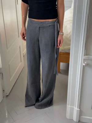 Grå vida linnebyxor med knytband - Snygga grå linnebyxor med hög midja och vida ben. Byxorna har ett stilrent knytband i midjan som detalj och är tillverkade i ett luftigt linnematerial. Perfekta för en avslappnad och trendig look. Andvända 3 ggr